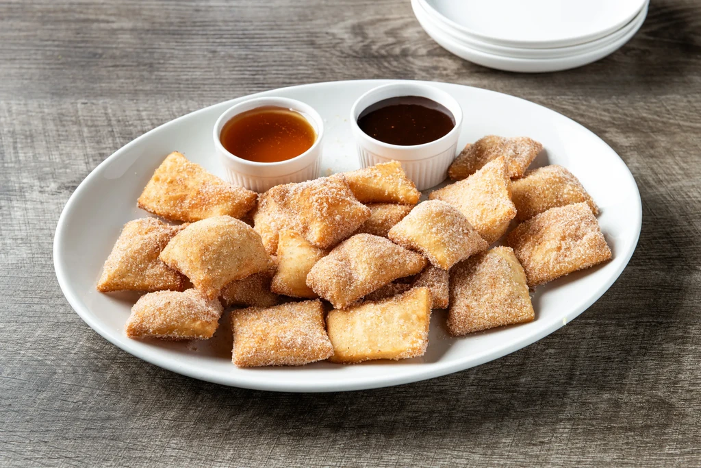 Platter of golden-brown fried pastries coated in sugar, with two dipping sauces.