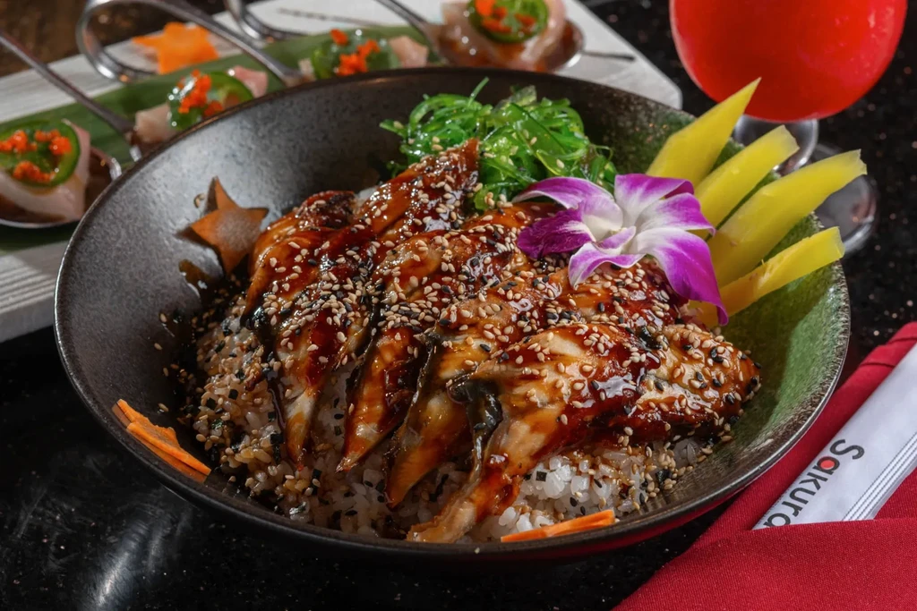 Close-up: Unagi Don, wakame, orchid, appetizers, dark restaurant table.