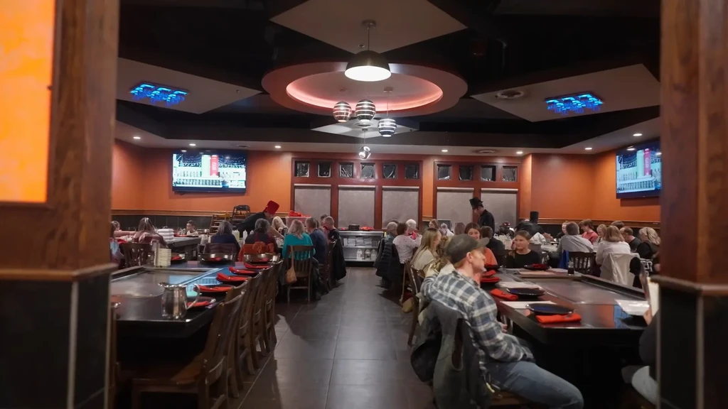 Bustling hibachi restaurant interior with customers and chefs.
