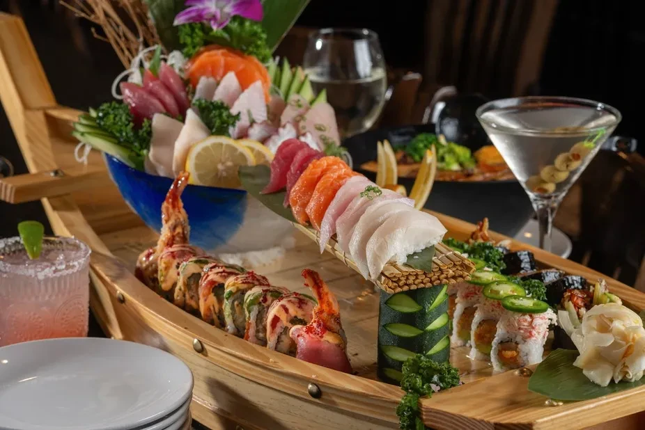 Sushi and sashimi boat with various rolls and foreground cocktails.