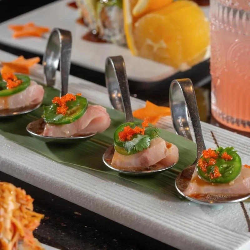 Four sashimi appetizers topped with jalapeño, tobiko, cilantro on spoons.