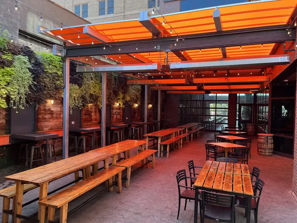 Empty restaurant patio with rustic tables, orange canopy, and green living wall.