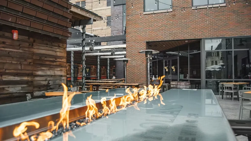 Modern elongated fire pit with flames on an outdoor restaurant patio.