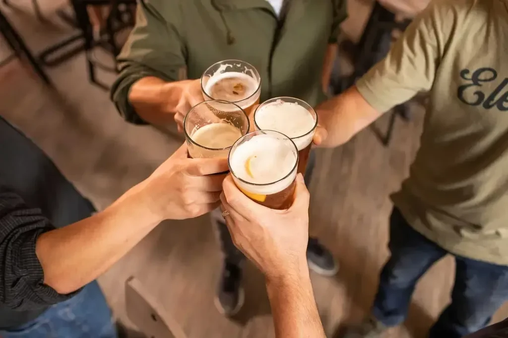 Four hands toast diverse beers with a lemon slice in a bar.