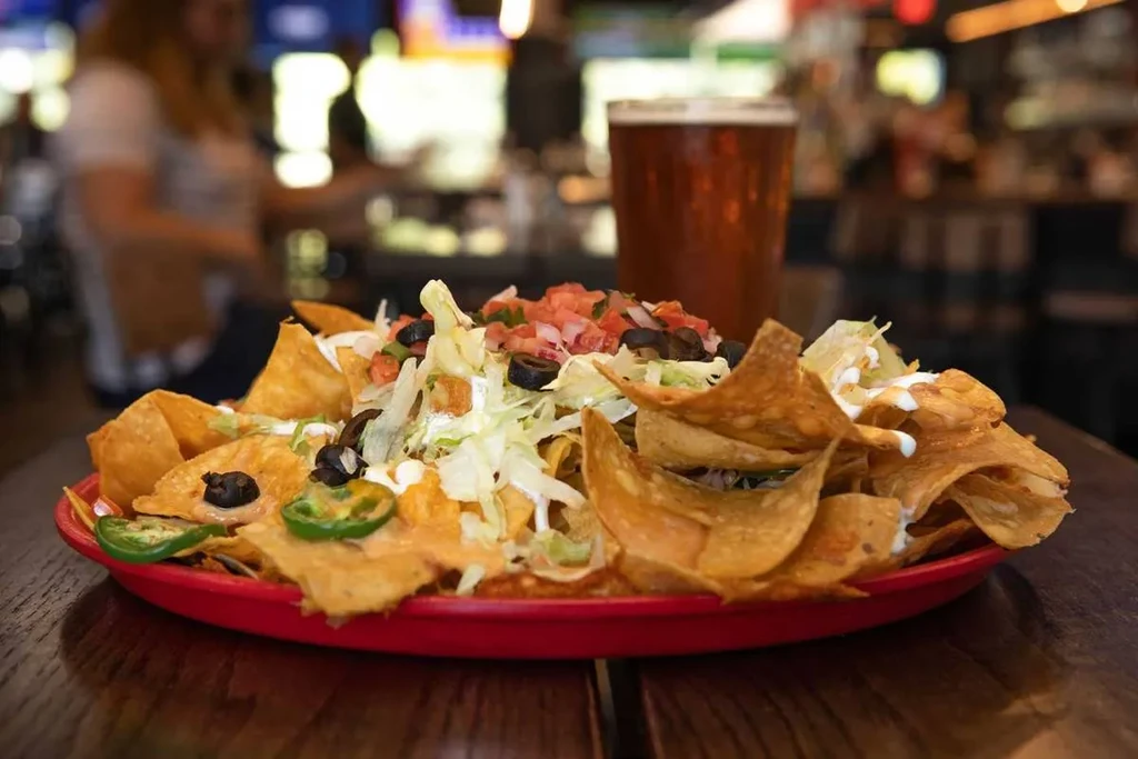 A large plate of fully loaded nachos with cheese, jalapeños, and beer.