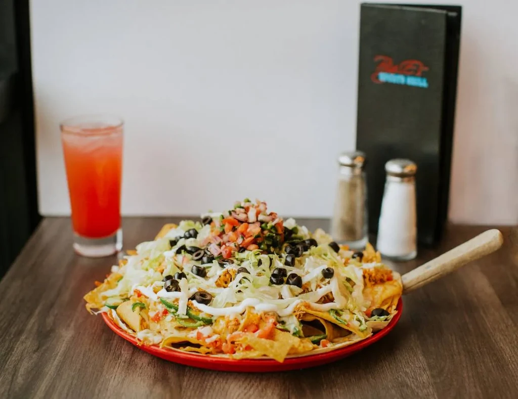 Plate of loaded nachos with a drink and menu on a wooden table.