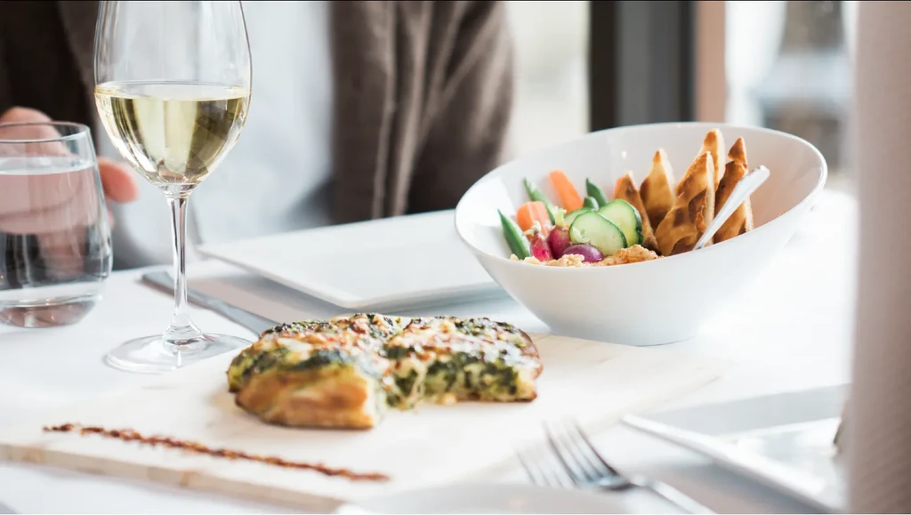Restaurant table with savory tart, wine, salad, and person's hands.