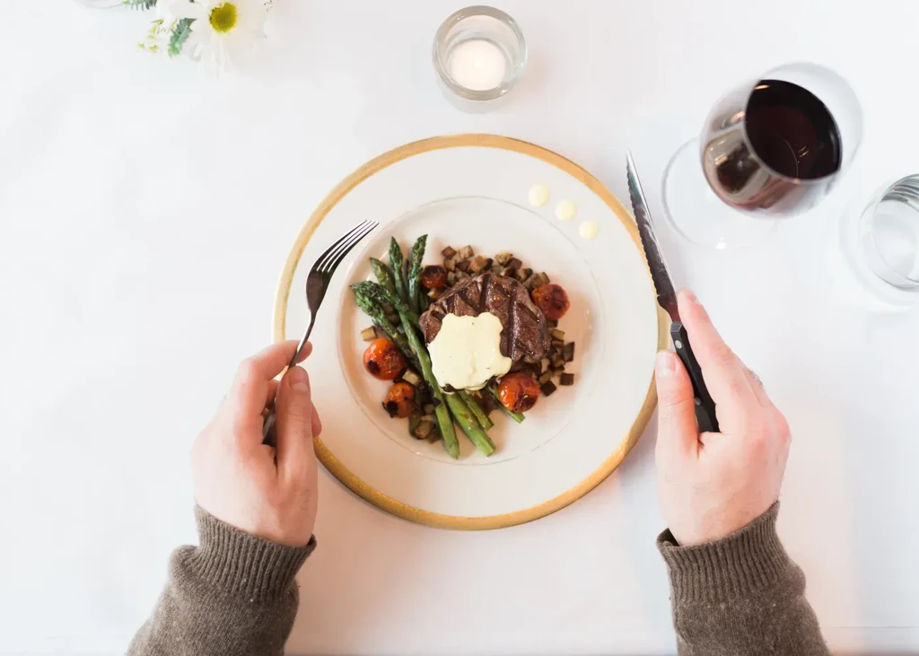 Overhead shot: Plated steak, asparagus, and tomatoes with fork and knife.