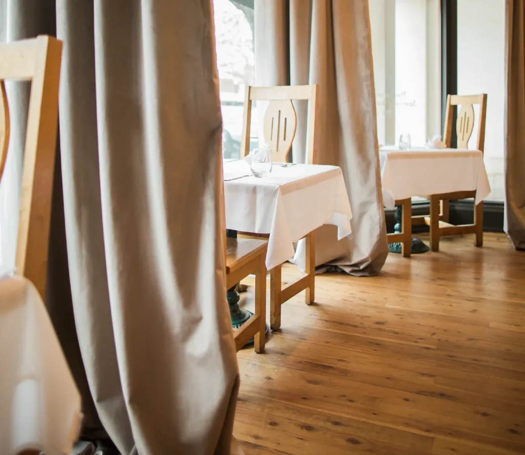 Restaurant dining area with wooden tables, white tablecloths, and divider curtains.