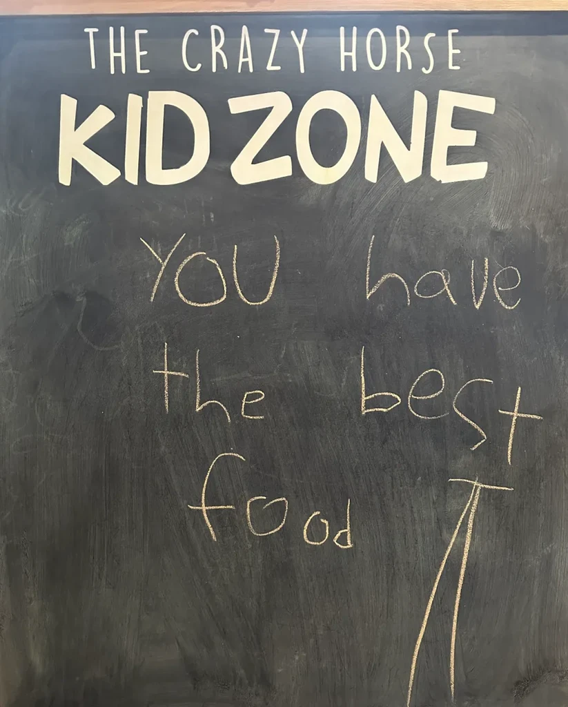 Blackboard sign: "THE CRAZY HORSE KID ZONE" and "YOU have the best food".