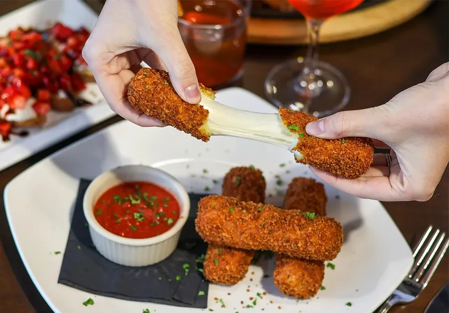 Hands pull apart a mozzarella stick, showing stretchy cheese, with red sauce.