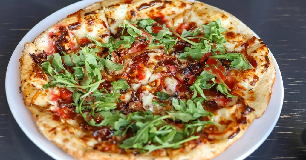 Pizza with melted cheese, caramelized onions, red drizzle, and fresh arugula.