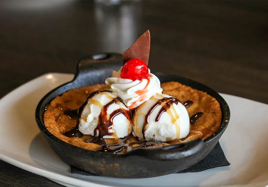 Skillet cookie topped with vanilla ice cream, sauces, whipped cream, and cherry.