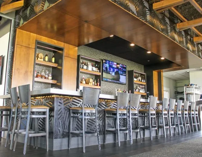 Modern bar with geometric counter, liquor, TV, and copper overhead structure.