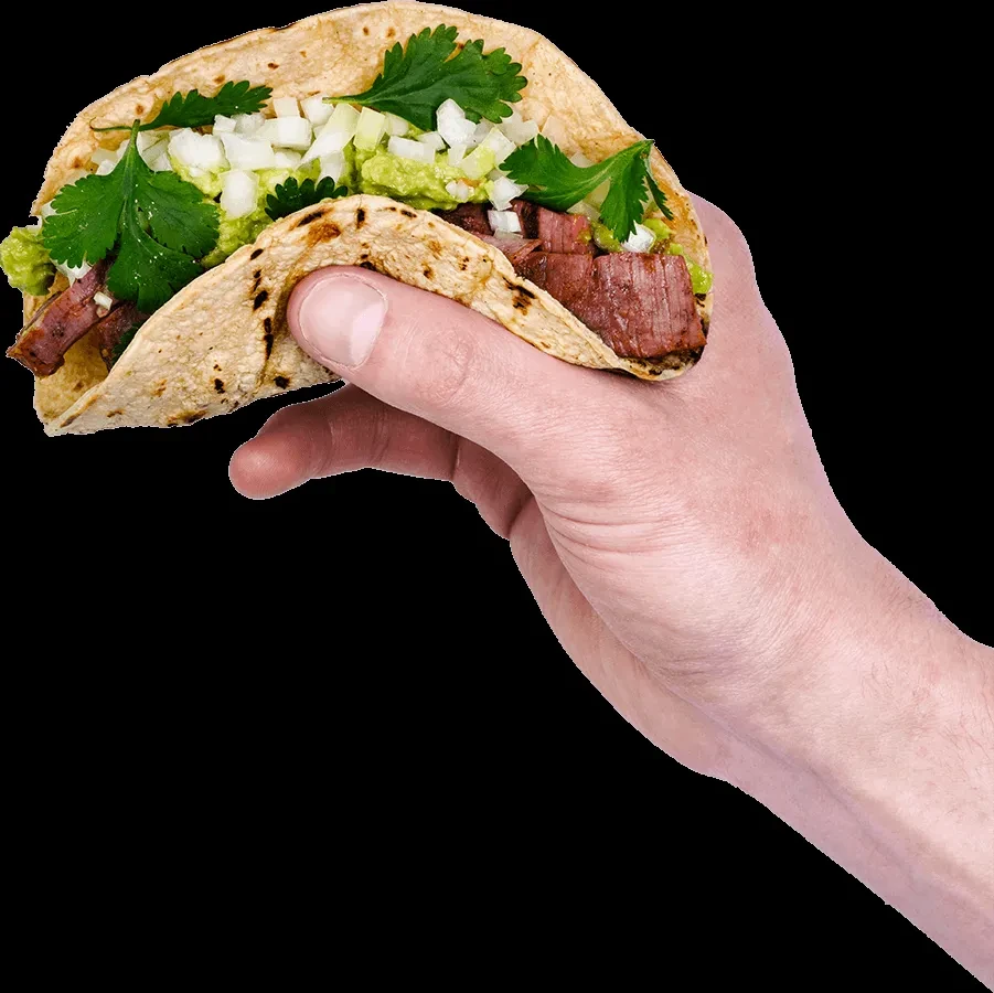 Hand holding a grilled meat taco with guacamole, onions, and cilantro.