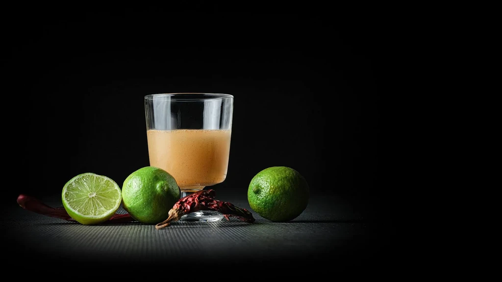 Frothy brown liquid, limes, and red chilies on a dark surface.