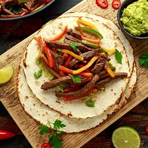 Beef fajitas on stacked tortillas with peppers and guacamole.