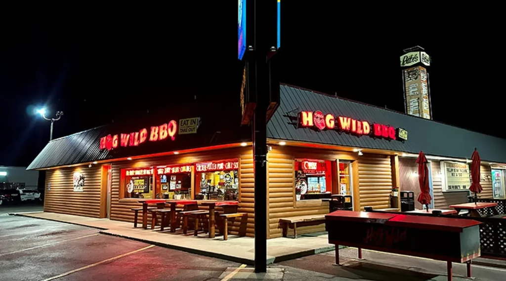 Hog Wild BBQ: rustic log cabin exterior with bright neon signs at night.