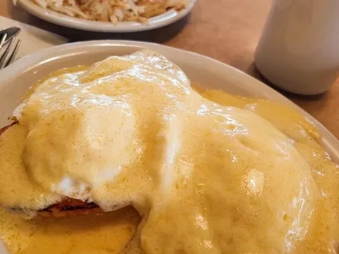 Eggs Benedict smothered in thick, frothy Hollandaise sauce on a white plate.