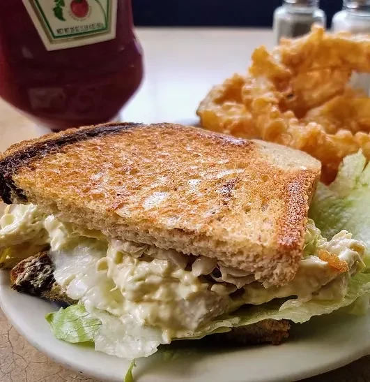 Toasted chicken salad sandwich, golden fries, and ketchup on a plate.