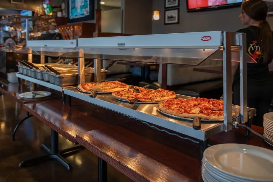 Three pizzas in a heated food warmer on a self-serve buffet.