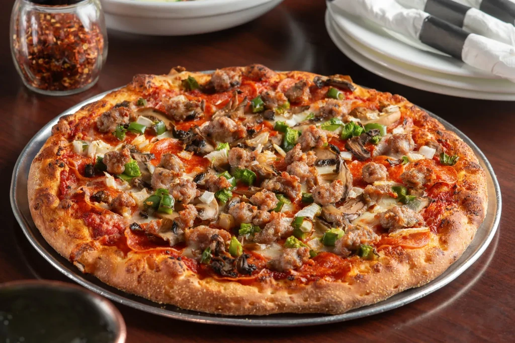 Freshly baked pizza with sausage, pepperoni, cheese, and vegetable toppings.