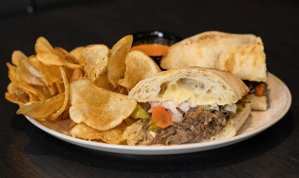 Pulled meat sandwich with melted cheese, pickled vegetables, chips, and dipping sauce.