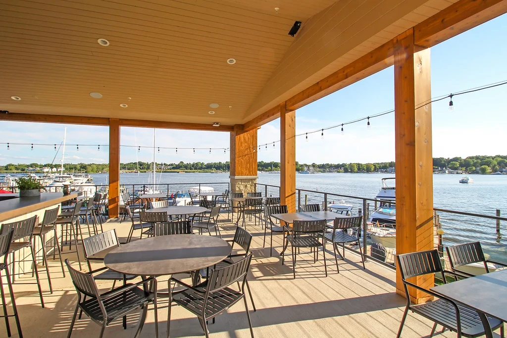 Covered restaurant patio with empty tables, string lights, and lake view.