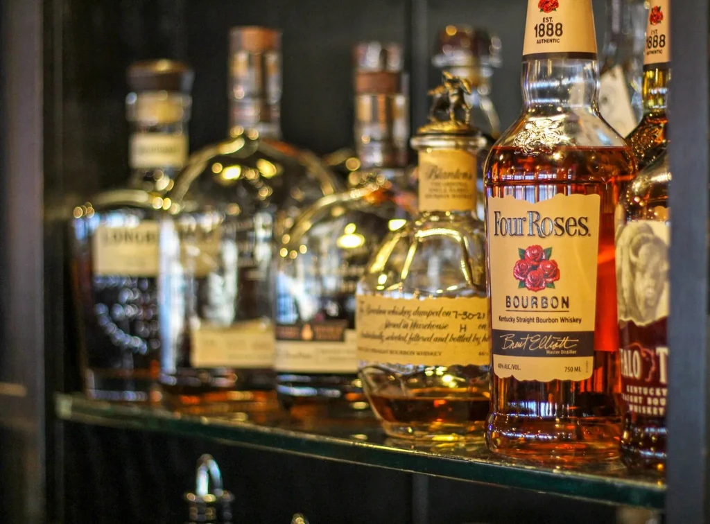 Four Roses Bourbon bottle in focus, blurred whiskey bottles on a shelf.