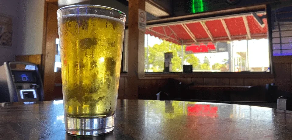 Frosted beer glass on bar, ATM and window visible.