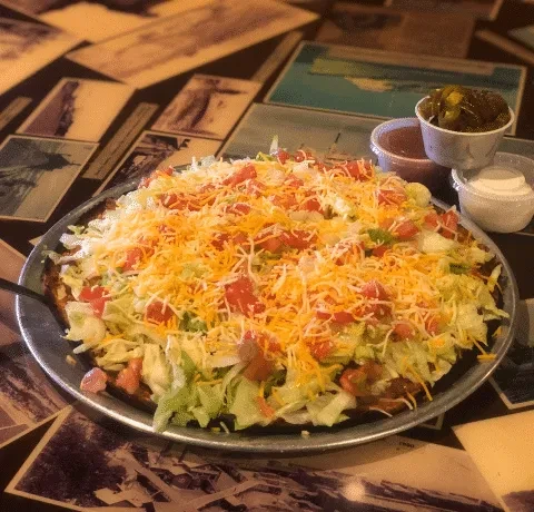 Large nachos or taco pizza with lettuce, tomatoes, cheese, condiments.