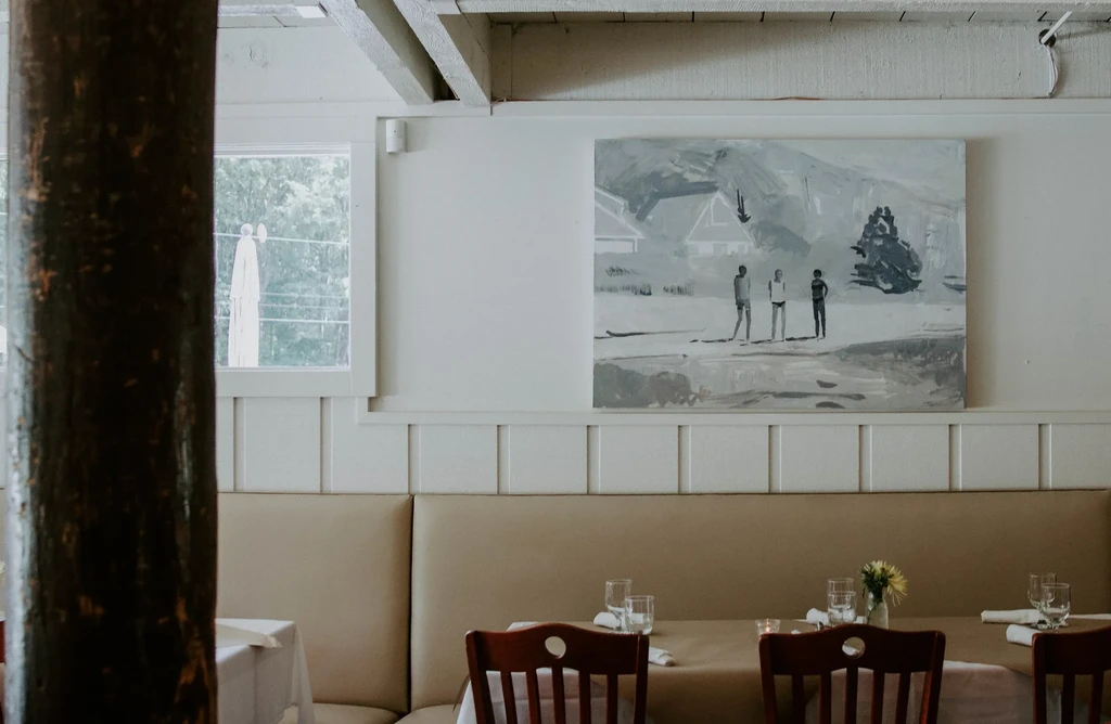Empty restaurant dining room with banquette, tables, and landscape art.