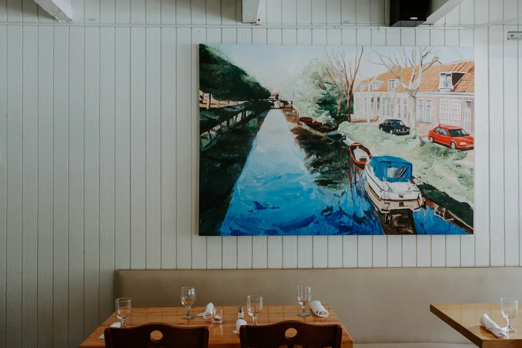Vibrant canal painting, wood-paneled wall, and set dining tables in restaurant.