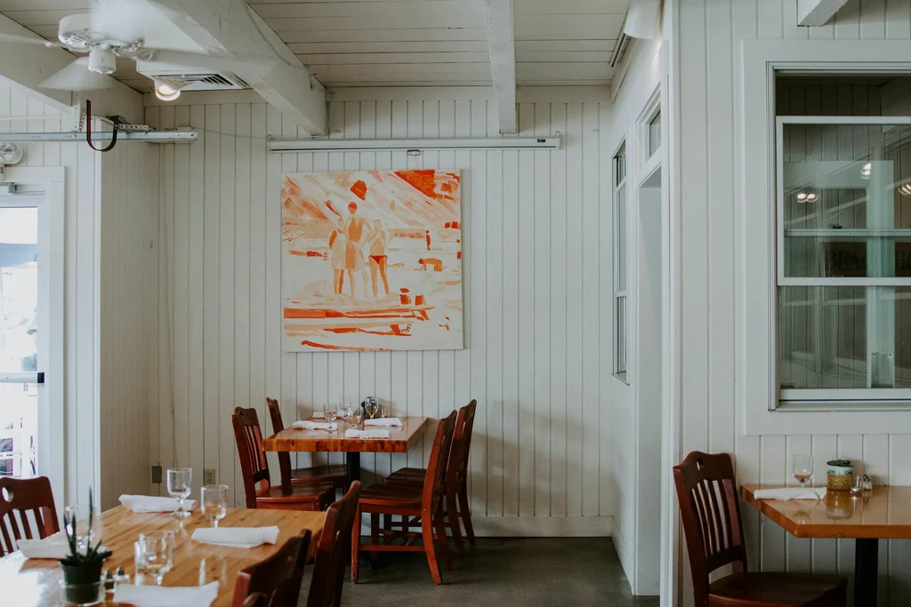 Bright, clean restaurant with wooden tables, white walls, and abstract art.