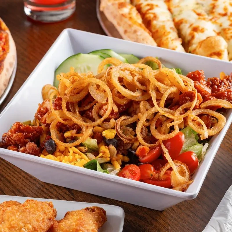 Vibrant salad topped with fried onion rings, fried chicken, and breadsticks.