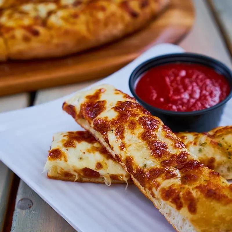 Two golden-brown cheesy breadsticks with red dipping sauce on a white plate.