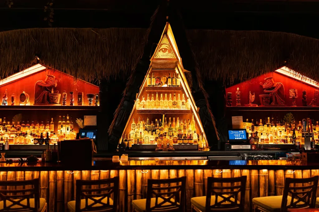 Tiki-style bar with backlit bottles, carved panels, and an all-seeing eye.