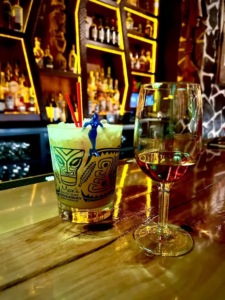 Two drinks on a tiki bar counter in a dimly lit bar.