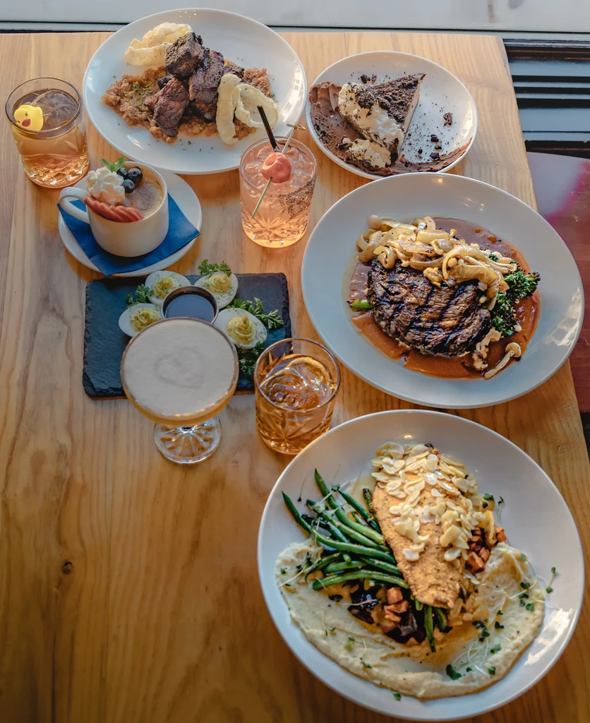 Dining table laden with gourmet steak, fish, desserts, cocktails, and other dishes.