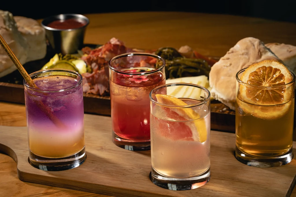 Four distinct colorful cocktails on a wooden board with charcuterie.