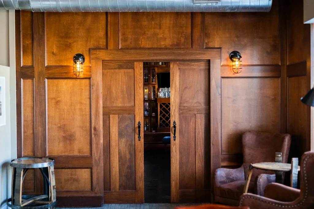 Warm wood wall, open bar doorway, industrial lighting, and lounge seating.
