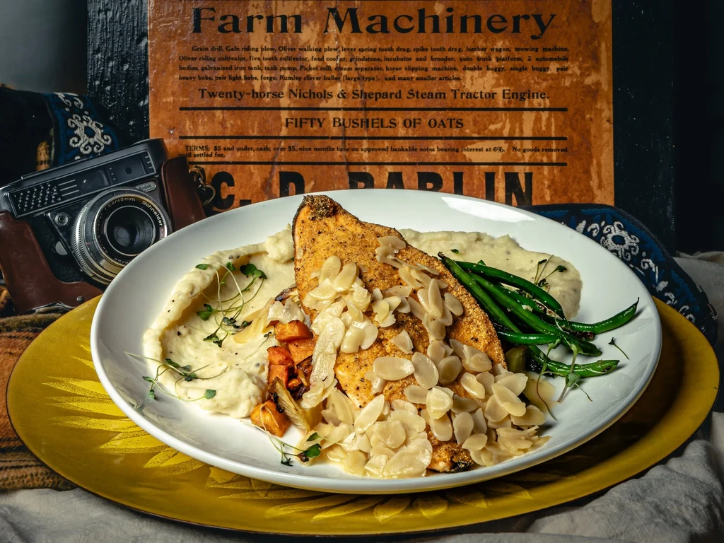 Plated fish/chicken, almonds, vegetables, vintage camera, and farm machinery sign.