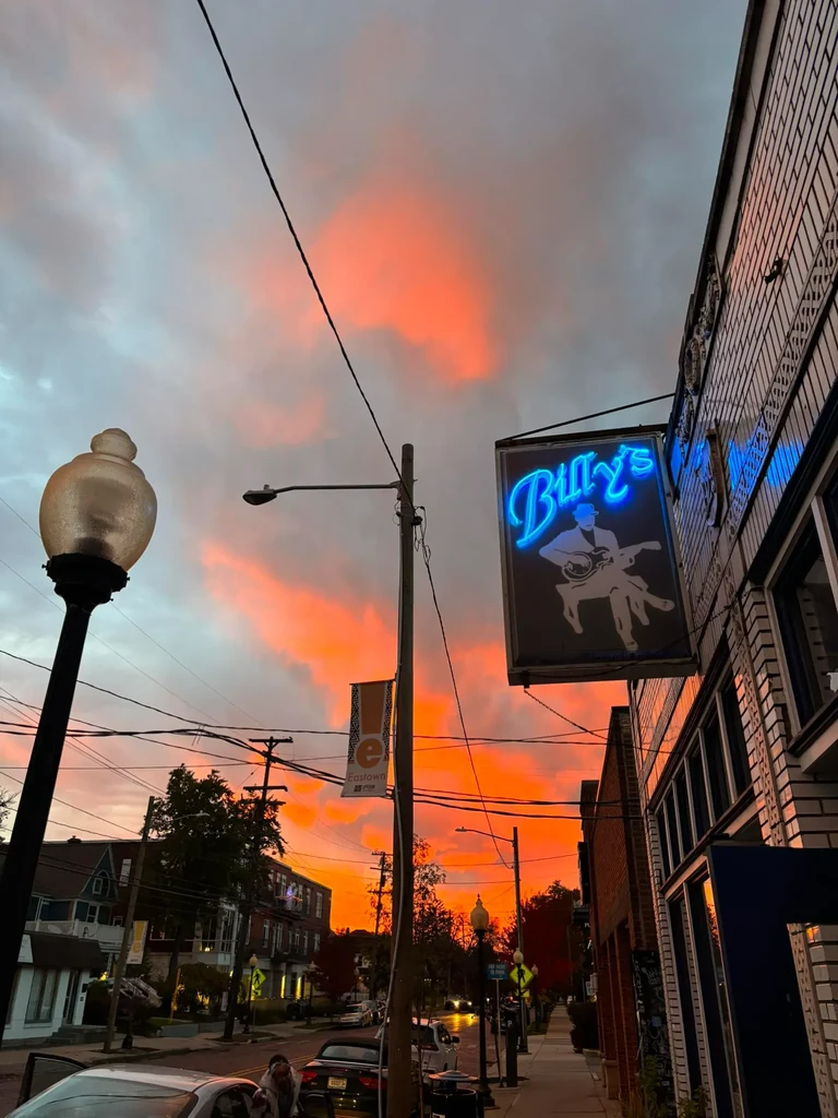 Street scene at sunset with Billy's neon musician sign and Eastown banner.