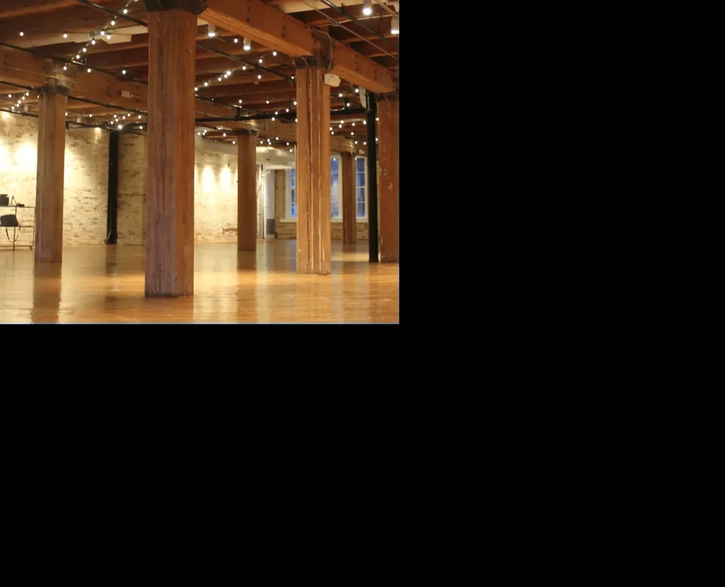 Empty rustic hall with wooden pillars, string lights, and reflective floor.