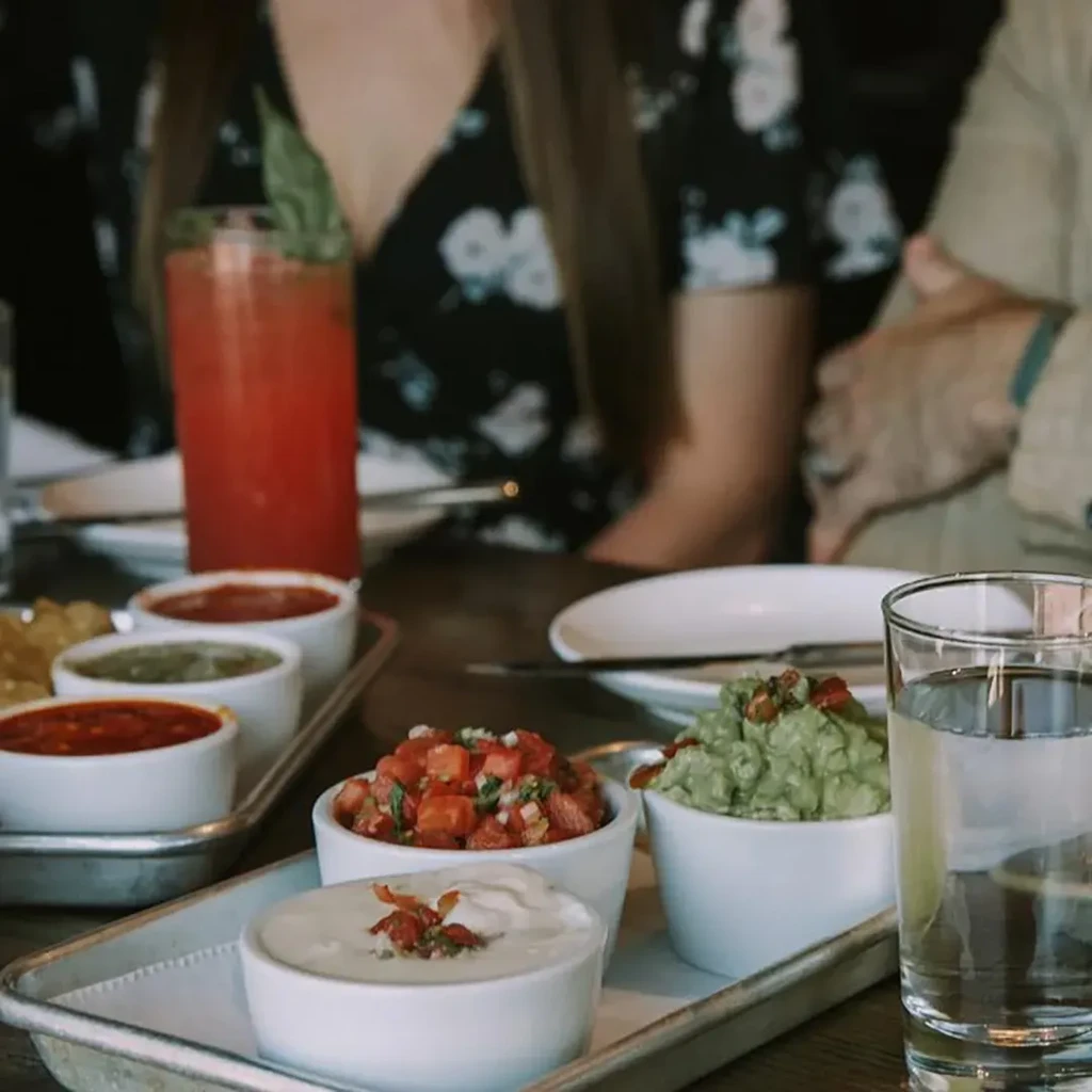 Rustic tray of dips, drinks, and blurred people at a table.