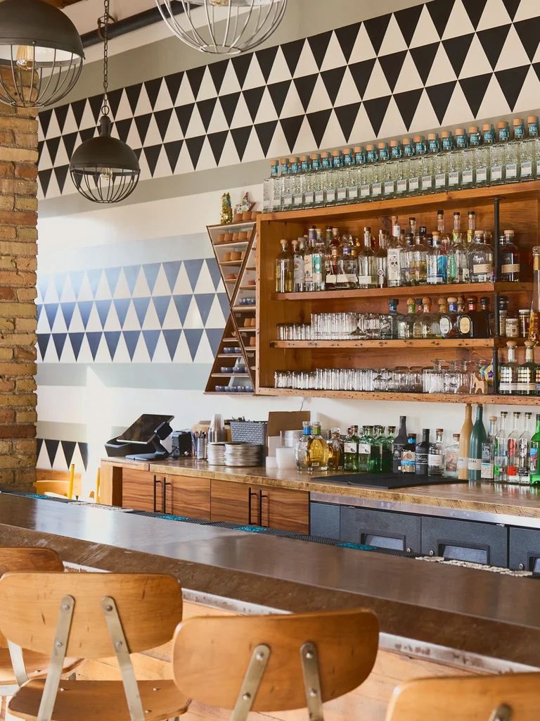 Empty modern bar with stocked shelves, stools, and geometric wall pattern.
