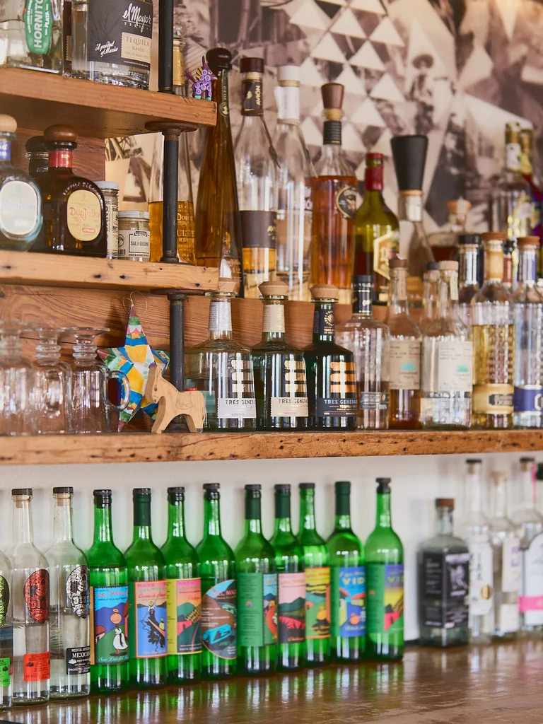 Rows of diverse spirits, like tequila and mezcal, on wooden shelves.