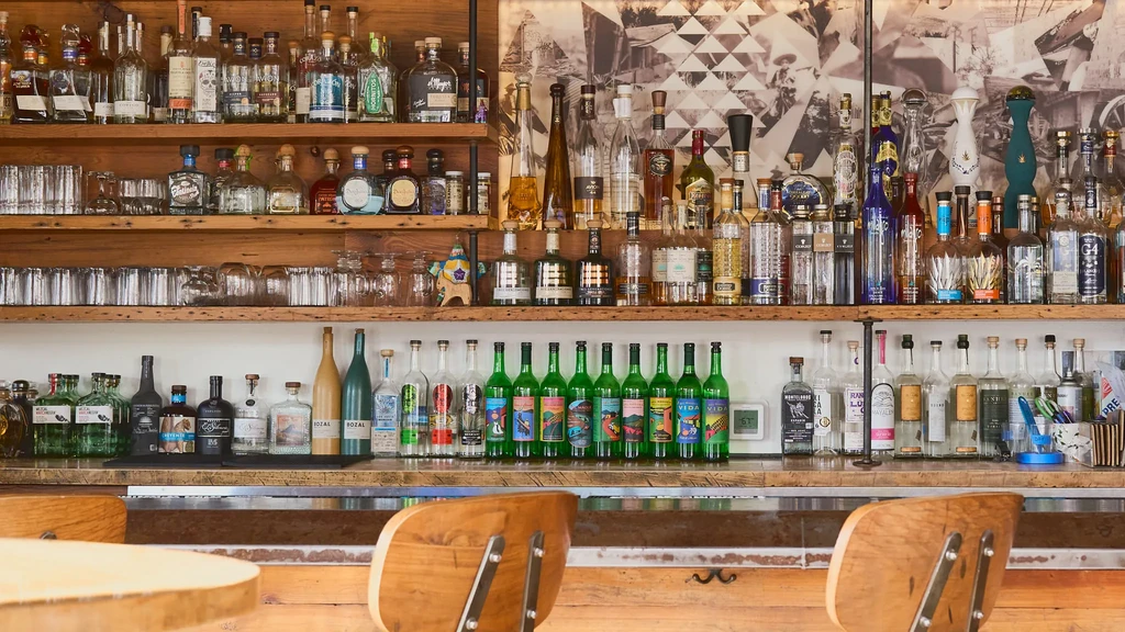 Extensive collection of spirit bottles on wooden shelves at a bar.