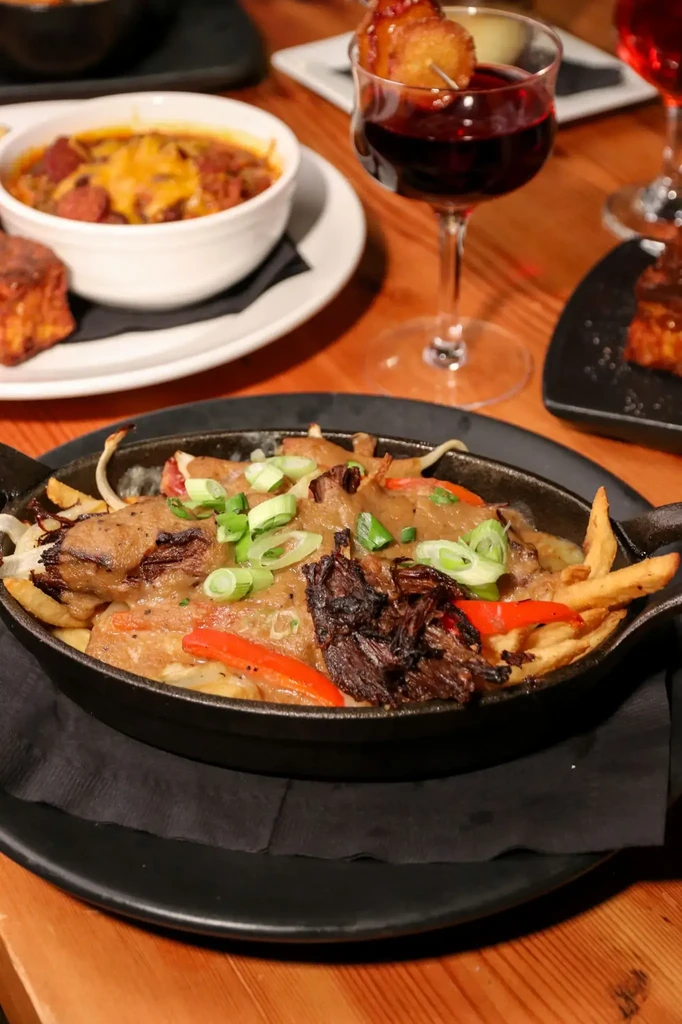 Hearty poutine skillet, chili, and drinks on rustic wood.