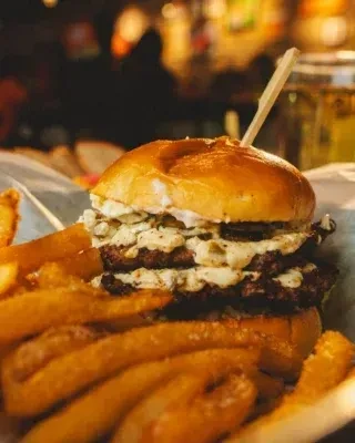 Close-up, well-lit double-patty burger with curly fries and skewer.